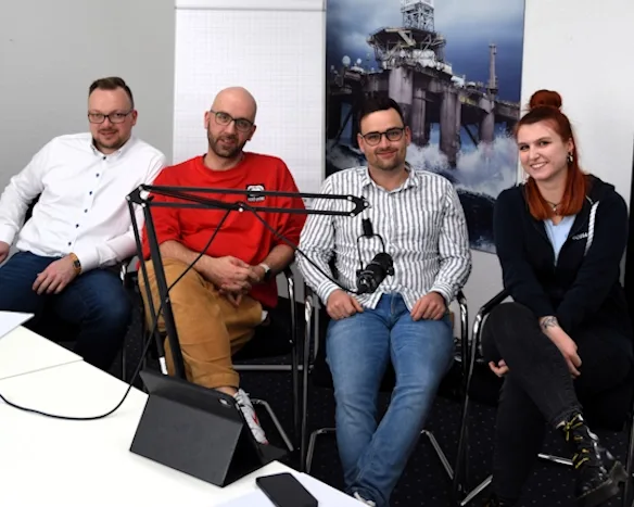 Zwei Podcast-Moderatoren und 2 Gäste sitzen an einem Tisch mit Mikrofonen, im Hintergrund eine Offshore-Plattform