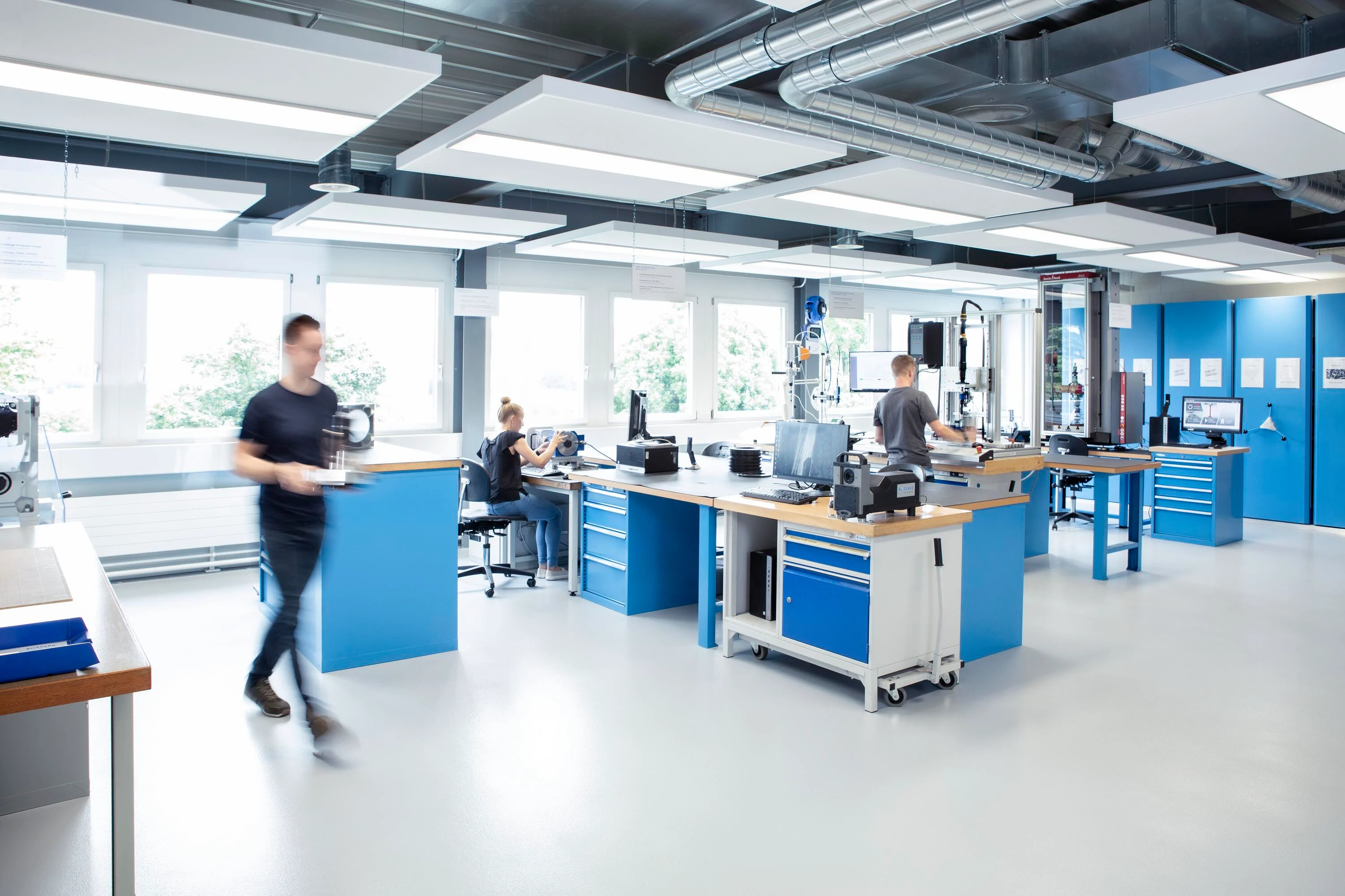 Tre ingeniører samarbejder om forskellige tests i et veludstyret laboratorium, med et klart overblik over både teamet og testudstyret.