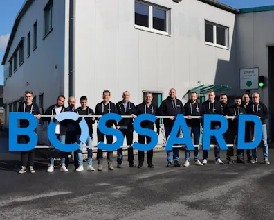 Team Bossard Velbert hält ein großes Bossard-Logo vor dem Firmengebäude.