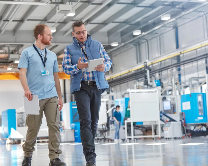 Zwei Fachkräfte mit Tablet diskutieren in einer Produktionshalle.