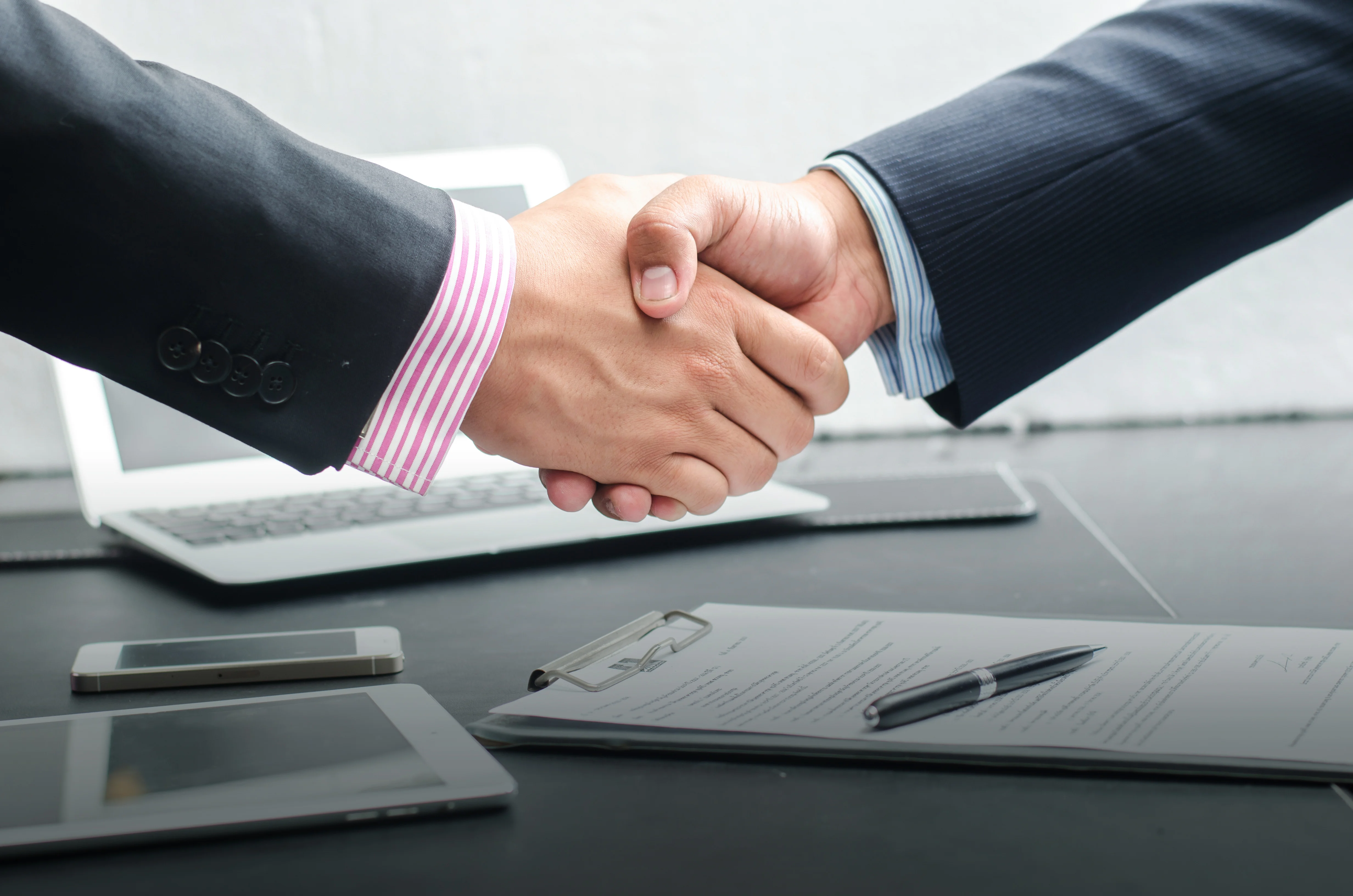 Zwei Geschäftsleute schütteln sich die Hände über einem Schreibtisch, symbolisieren Zusammenarbeit und Einigung.