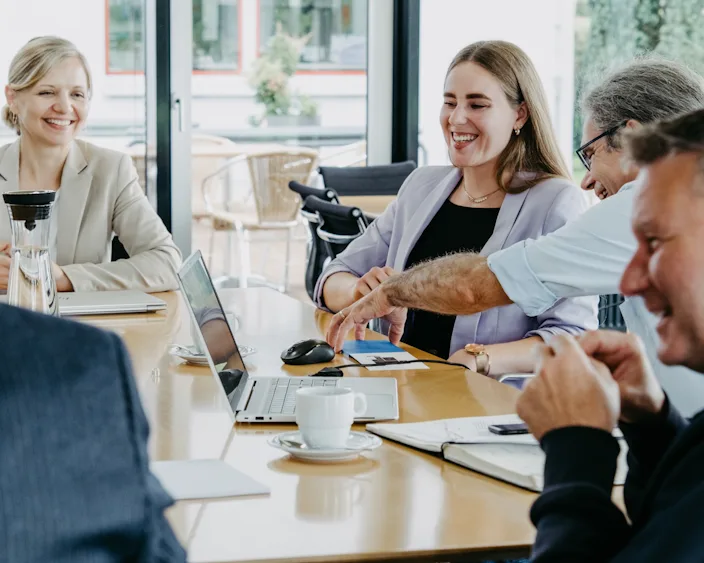 Bossard Mitarbeiter in einer Besprechung, lachen und diskutieren an einem Konferenztisch mit Laptop und Notizen.