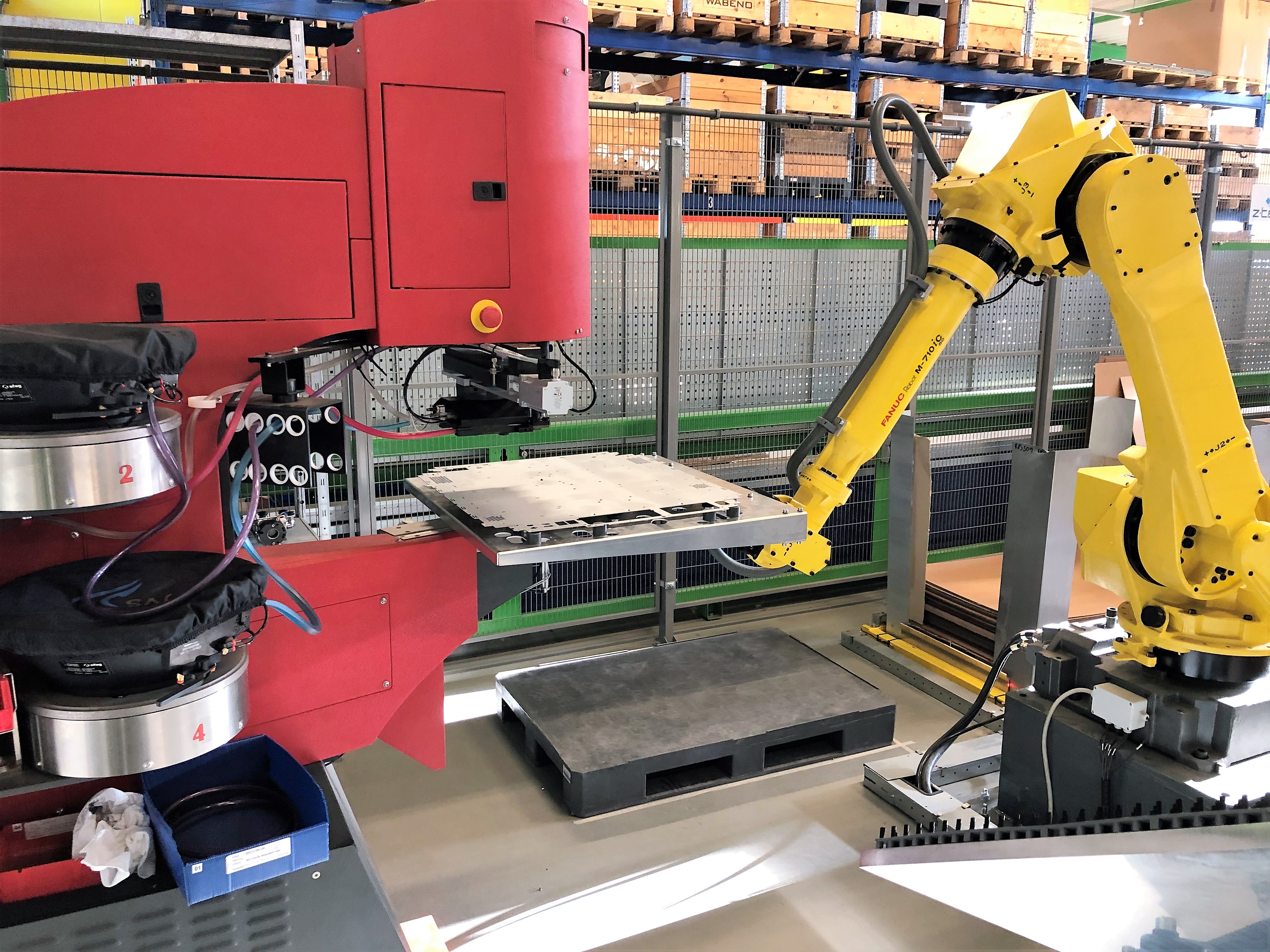 Eine rote Haeger-Einpressmaschine arbeitet mit einem gelben Roboterarm, um die Installation von Einpressbefestigern zu automatisieren.