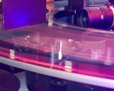 Nahaufnahme eines Prüfprozesses mit optischer Kamera und rot beleuchtetem Förderband