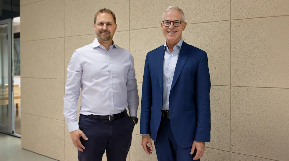 Florian Heuter im weißen Businesshemd auf der linken Seite, Frank Hilgers im blauen Anzug auf der rechten Seite, stehend vor einem hellbraunen Hintergrund.