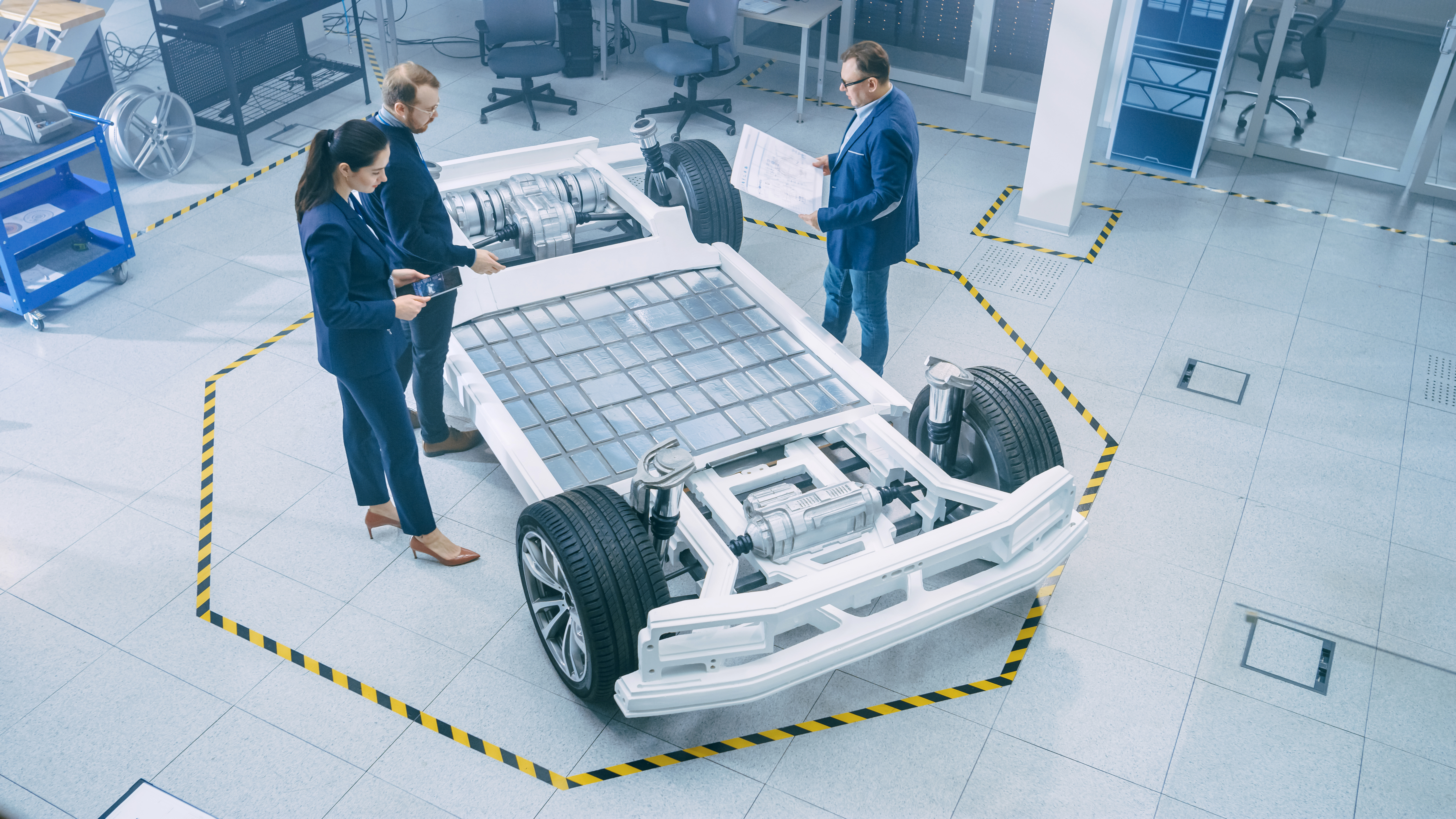 A woman and two men standing in front of an electric car chassis with solar panels.