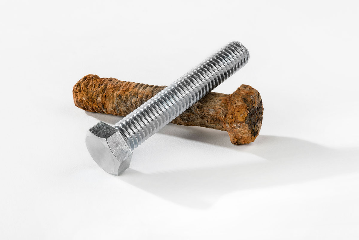 Eine metallische Schraube und eine korrodierte auf weissem Hintergrund, zur Veranschaulichung im Vergleich.