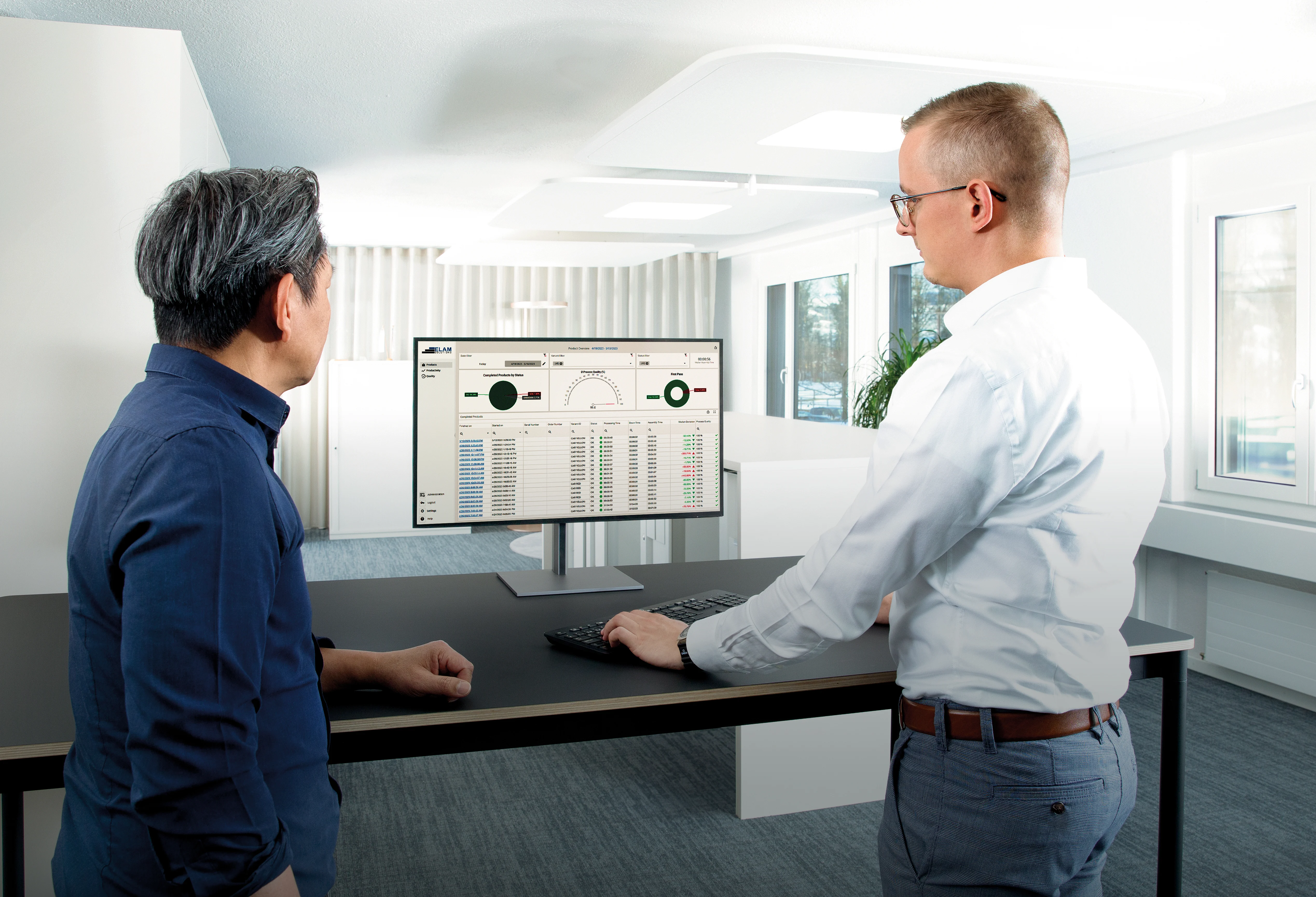 Two men at a desk, focused on a computer screen displaying a data report.
