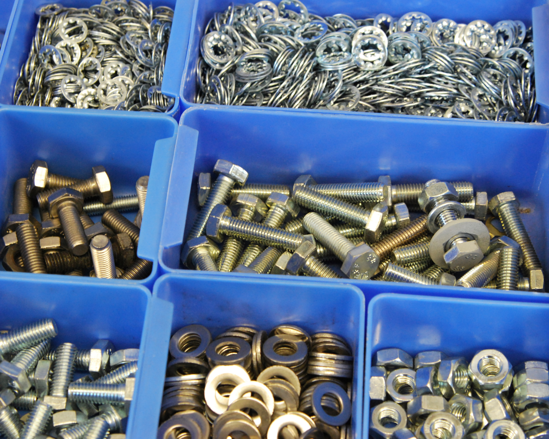 Blaue Sichtlagerkästen mit sortierten Metallteilen wie Schrauben, Muttern, Unterlegscheiben und Sicherungsringen.