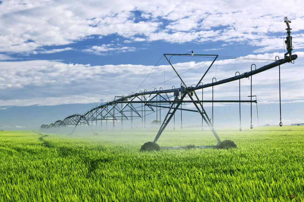 Linear irrigation system watering a green field with a blue sky with clouds in the background