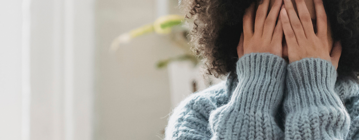Närbild på en person som täcker sitt ansikte med händerna.