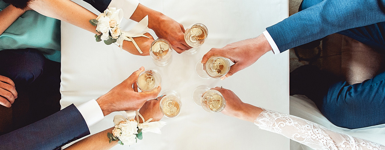 Ylhäältä otettu kuva häävieraista nostamassa kuohuviinimaljaa pöydän yllä.