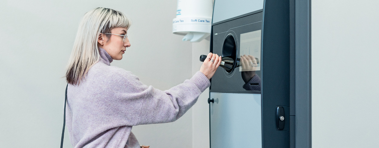 Nainen laittaa tyhjää lasipulloa pullonpalautusautomaattiin.