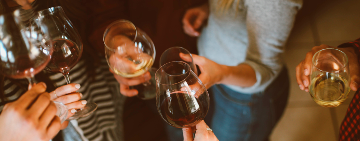 Närbild på personers händer som höjer en skål med vinglas.
