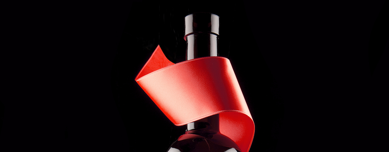 Lähikuva mustalla taustalla viinipullon kaulasta, jonka ympärillä on punainen satiininauha