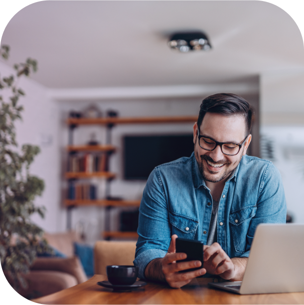 man at desk smiling with phone and laptop
