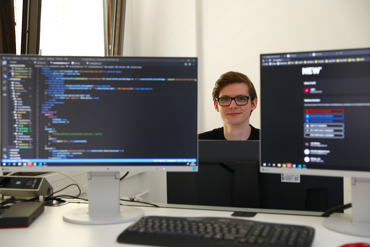 Moderner IT‑Arbeitsplatz im Rahmen der MATSE‑Ausbildung bei der NEW AG: Ein Schreibtisch mit zwei Monitoren zeigt auf der linken Seite Programmcode in einer Entwicklungsumgebung und auf der rechten Seite eine digitale Web‑ und Systemoberfläche im NEW‑Design. Die Arbeitsumgebung steht für praxisnahe Softwareentwicklung, moderne IT‑Ausbildung und die Verbindung von Theorie und Praxis z.B. im dualen Studiengang MATSE.