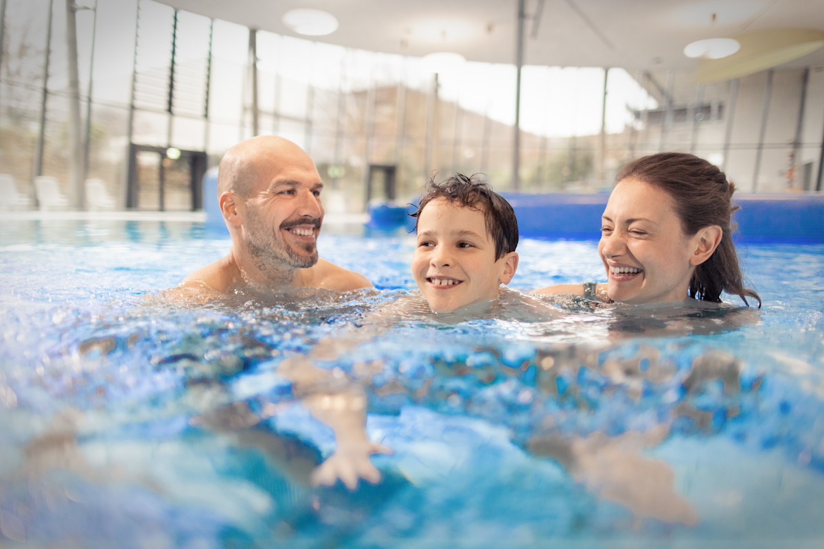 Ein lächelndes Ehepaar mit ihrem Kind im Freizeitbecken eines Schwimmbades