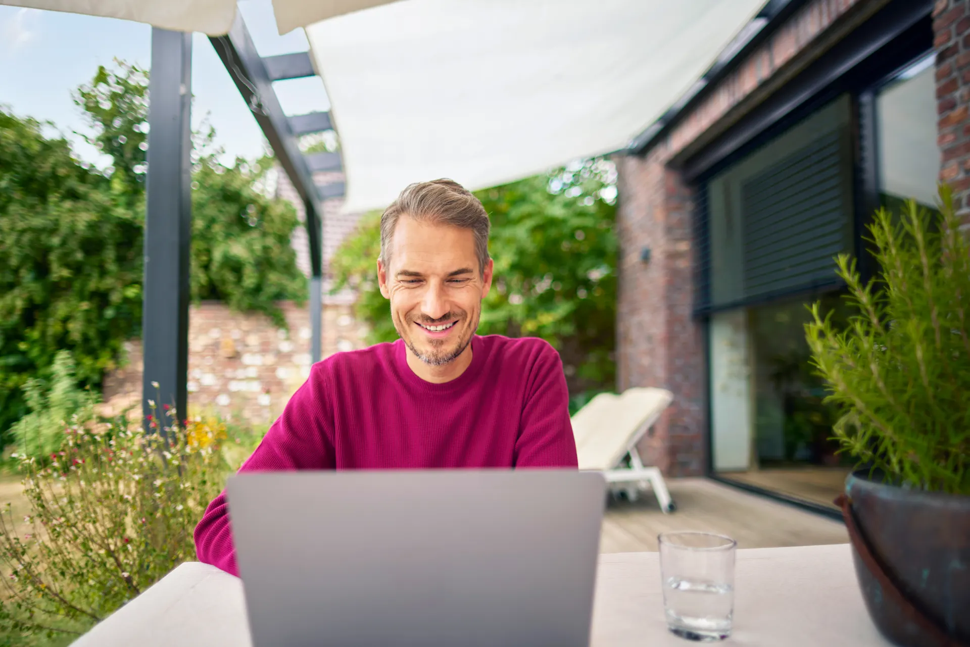 Ein Mann sitzt im Garten mit einem Laptop und informiert sich ueber Dienstleistungen der NEW Gruppe.