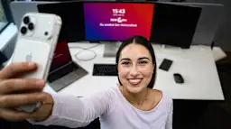 Vicky am modernen Arbeitsplatz - Selfie. Dieses Bild wurde mit Hilfe von KI erstellt Eine lächelnde junge Frau in weißem Langarmshirt macht ein Selfie mit ihrem Smartphone an ihrem modernen Arbeitsplatz. Auf dem Schreibtisch hinter ihr befinden sich ein großer Monitor mit buntem Farbverlauf-Bildschirmschoner, ein Laptop, eine Tastatur und weitere technische Geräte. Die Aufnahme zeigt eine Büro-Situation aus der Vogelperspektive. Dieses Bild wurde mit Hilfe von KI erstellt