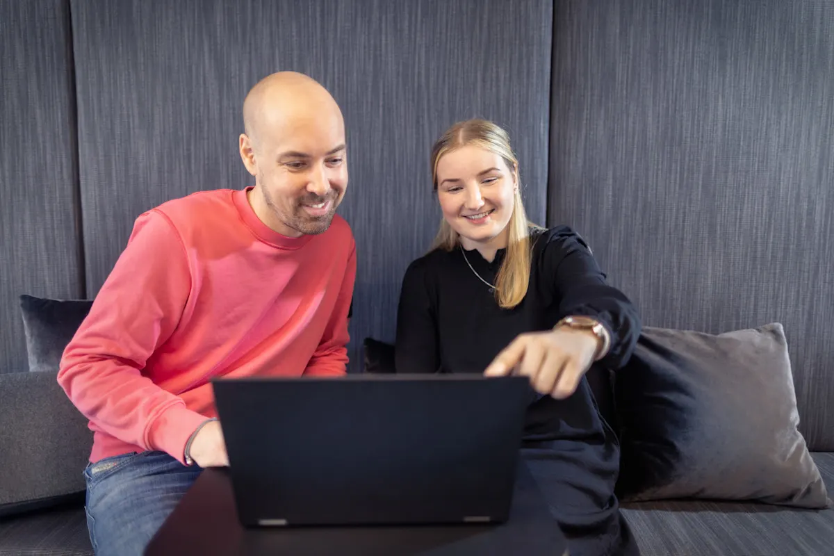 Zwei Kollegen sitzen zusammen und schauen auf einen Laptop.
