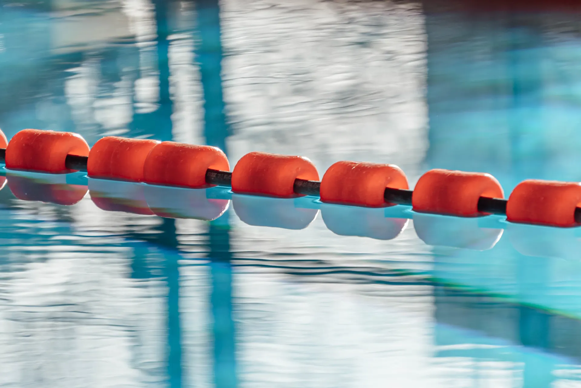 Schwimmkette Eine Nahaufnahme eines roten Bahnenabteilers mit mehreren orangefarbenen Schwimmern, die auf einer schwarzen Schnur auf dem Wasser ruhen.