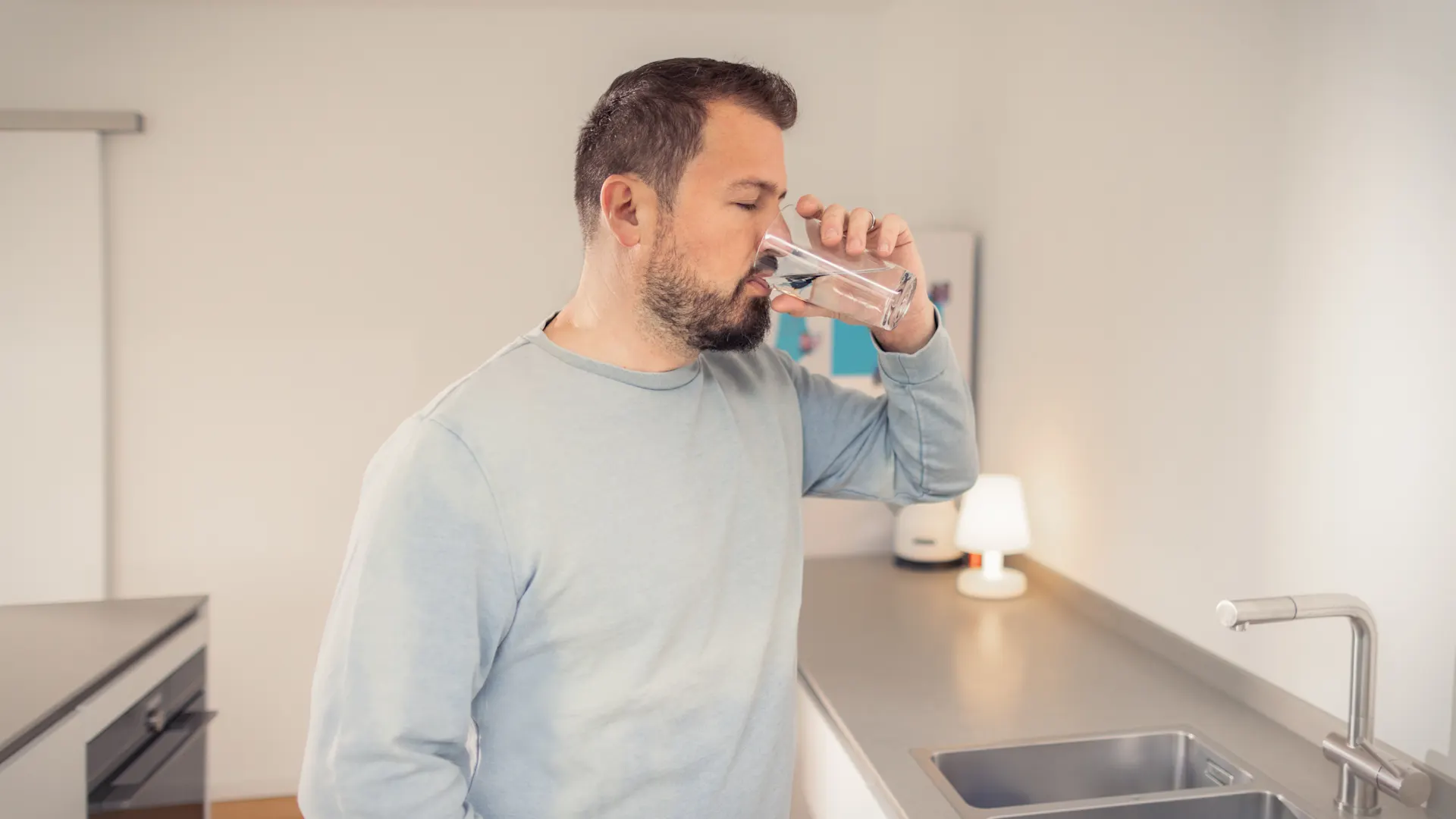 Trinkwasser - Lassen Sie Ihrem Durst freien Lauf Ein Mann steht in der Küche und trinkt Leitungswasser aus einem Glas