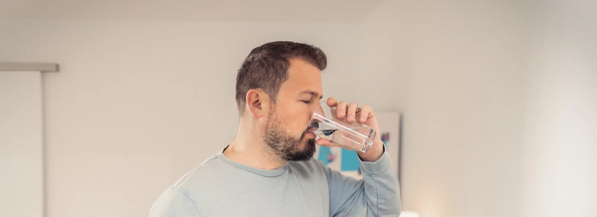 Trinkwasser - Lassen Sie Ihrem Durst freien Lauf Ein Mann steht in der Küche und trinkt Leitungswasser aus einem Glas