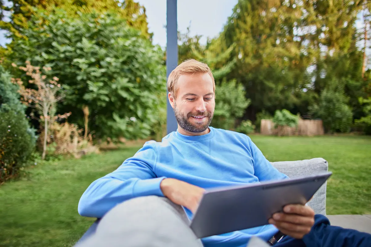Mann sitzt im Garten und schaut auf sein Tablet.