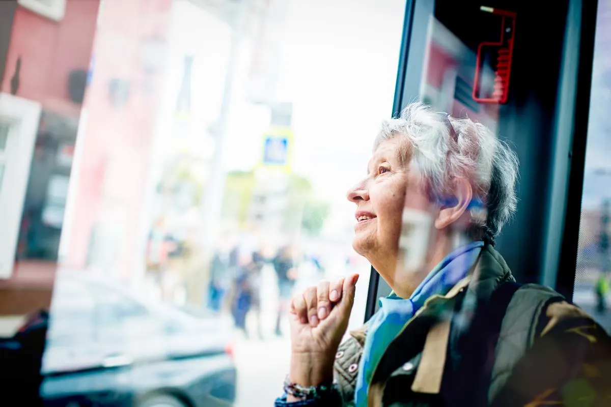 Ohne Auto mobil Ältere Dame im Bus, wie sie aus dem Fenster schaut.