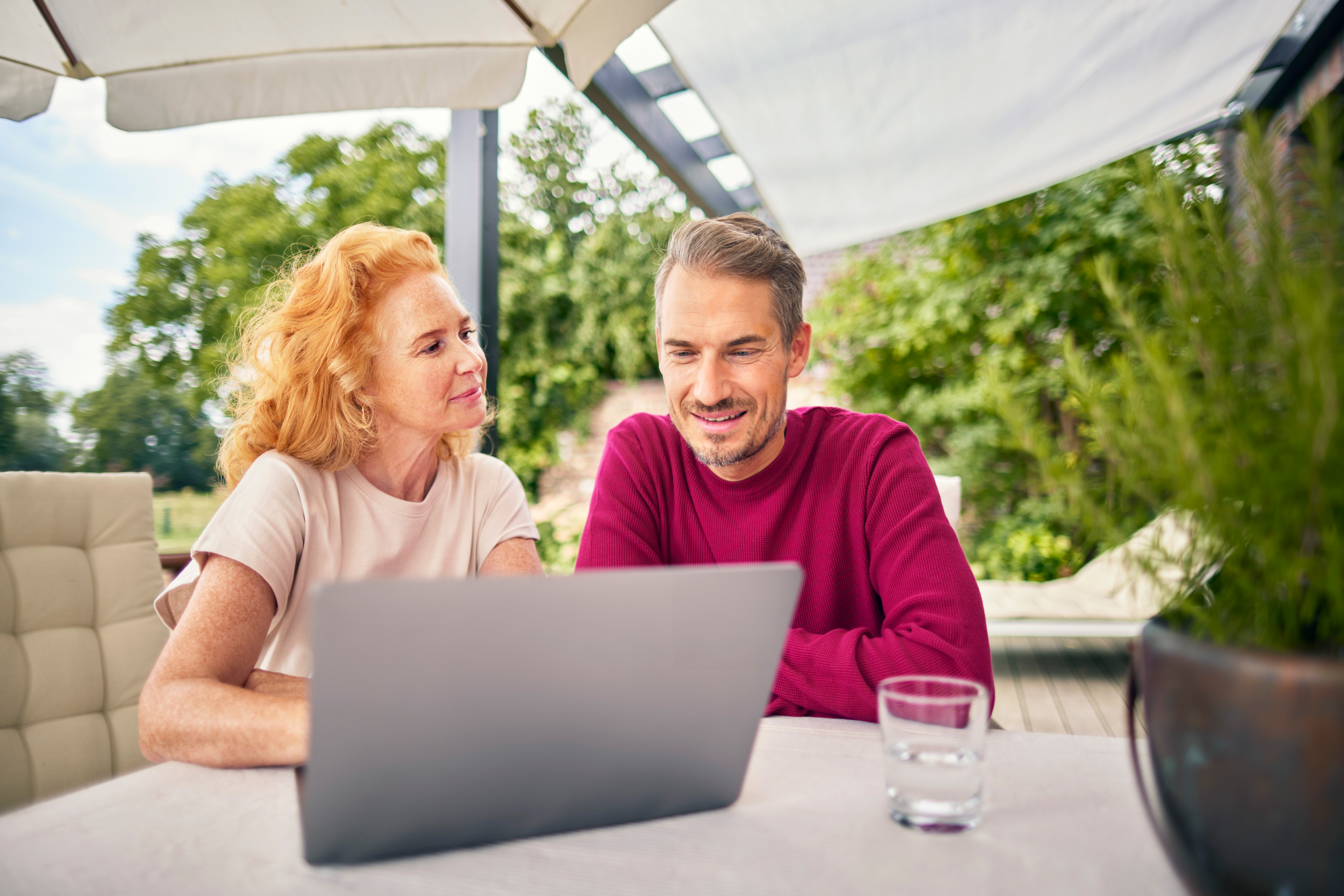 EIn Paar sitzt im Garten am Tisch vor dem Laptop 