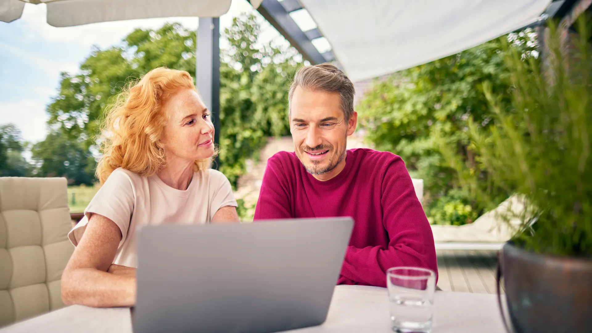 Ein Paar sitzt vor dem Laptop EIn Paar sitzt im Garten am Tisch vor dem Laptop