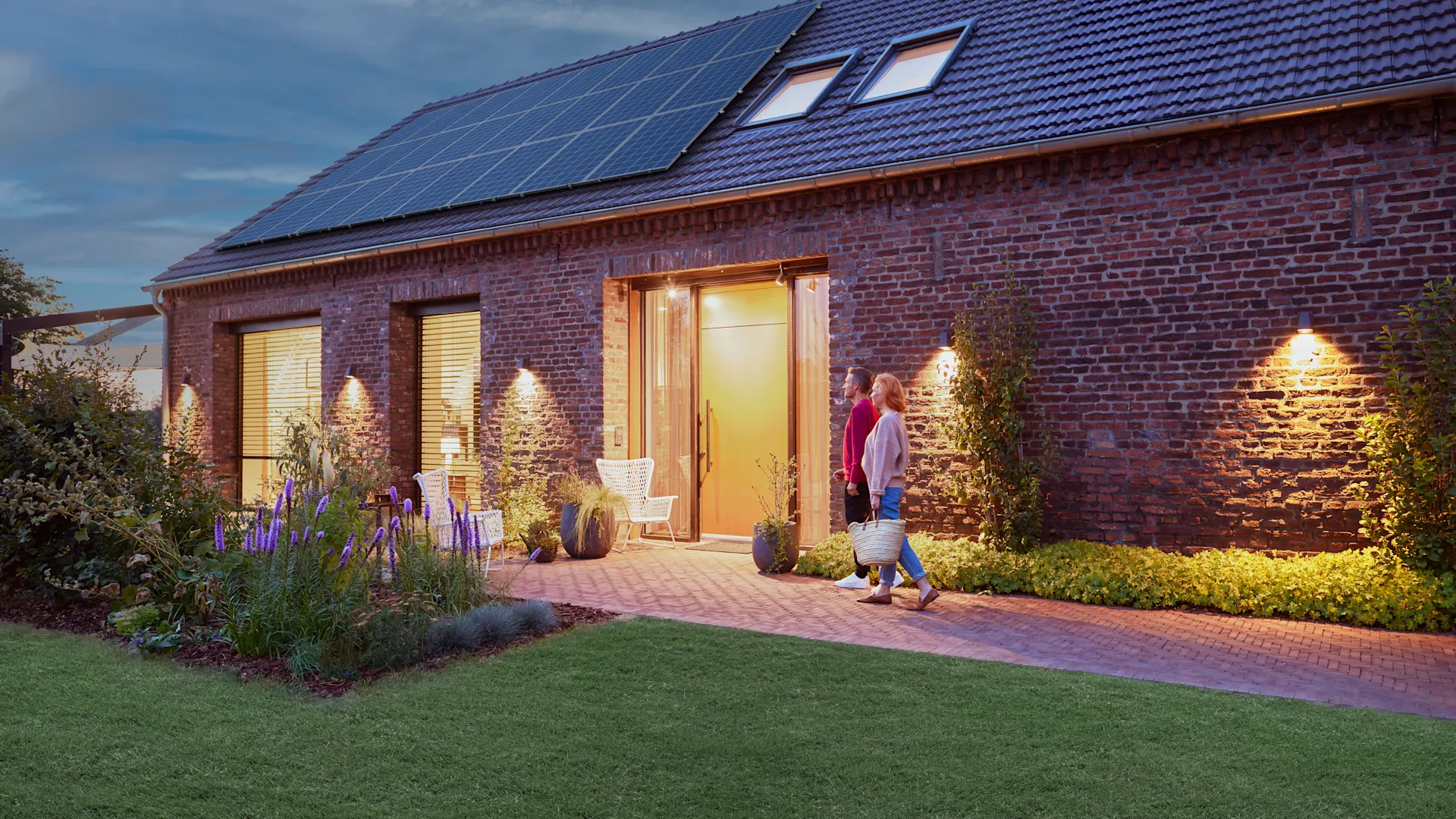 Photovoltaik bei Nacht Ein Einfamilienhaus auf dessen Dach eine Photovoltaikanlage zu sehen ist. Es ist Abenddämmerung und das Haus scheint hell erleuchtet.