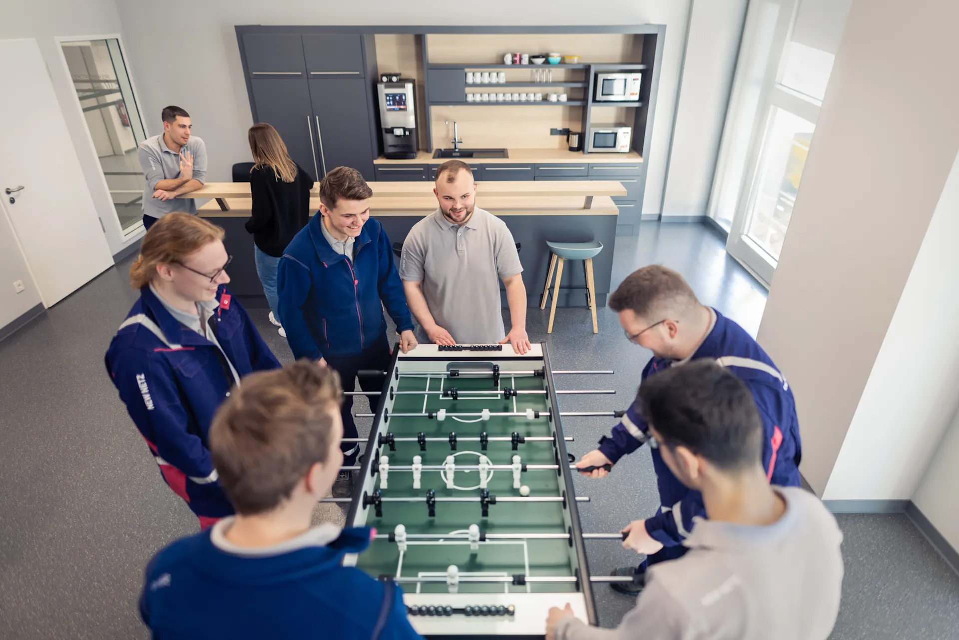 Auszubildene am Kickern Fünf Auszubildene der NEW Netz stehen um einen Kickertisch und genießen ihre Mittagspause beim Kickern in den Werkstätten der NEW Netz.