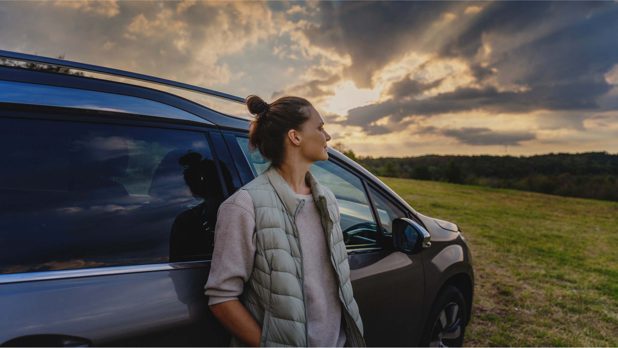 Frau lehnt an einem Auto und blickt in die Landschaft
