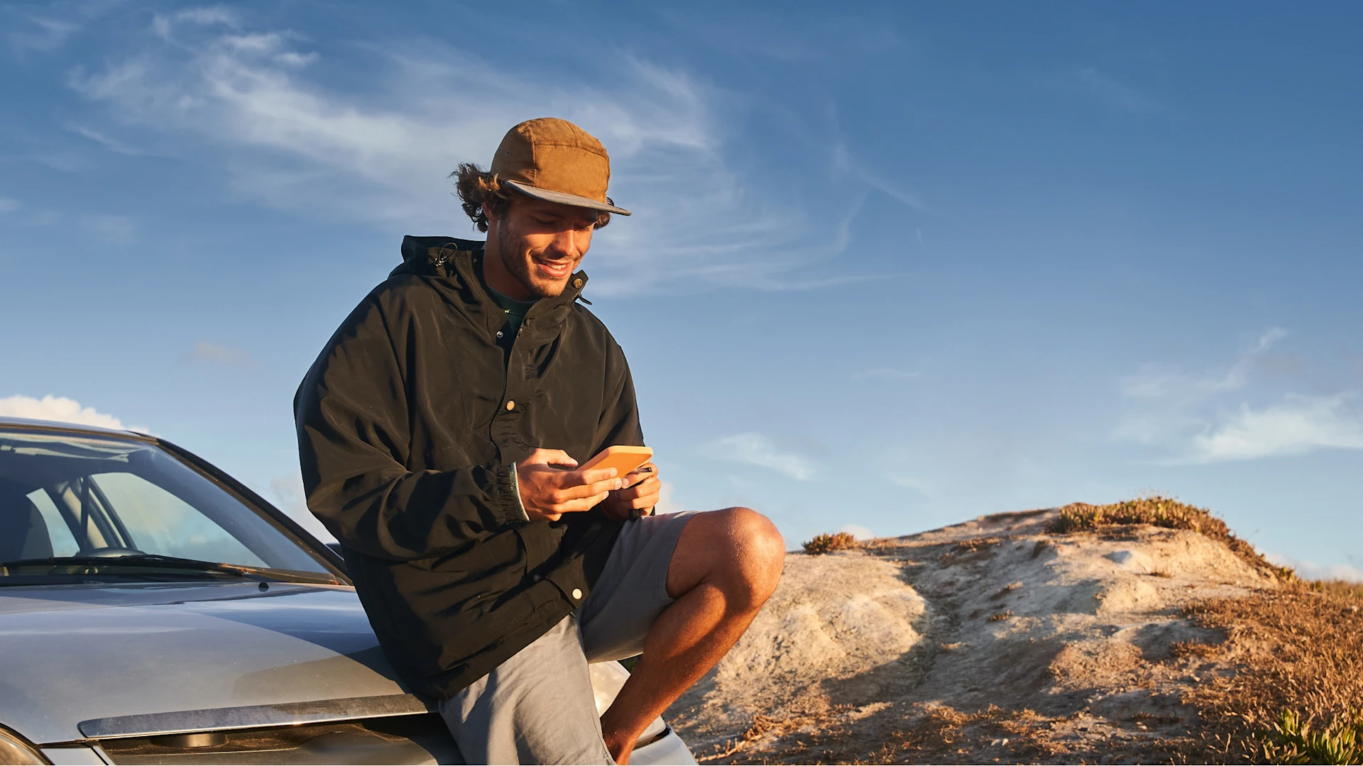 Mann mit Handy auf Motorhaube