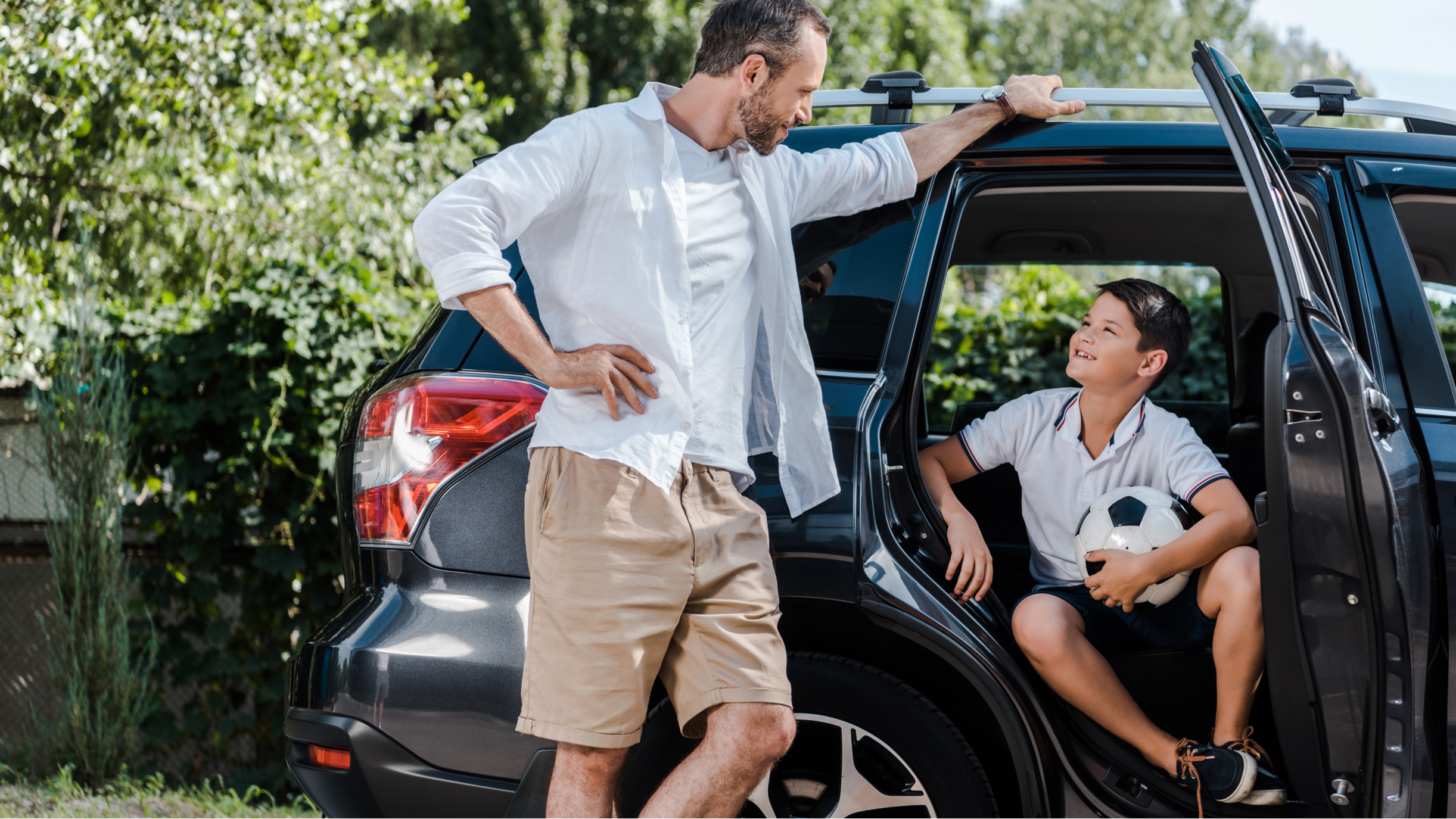 Mann lehnt am Auto und redet mit einem Kind