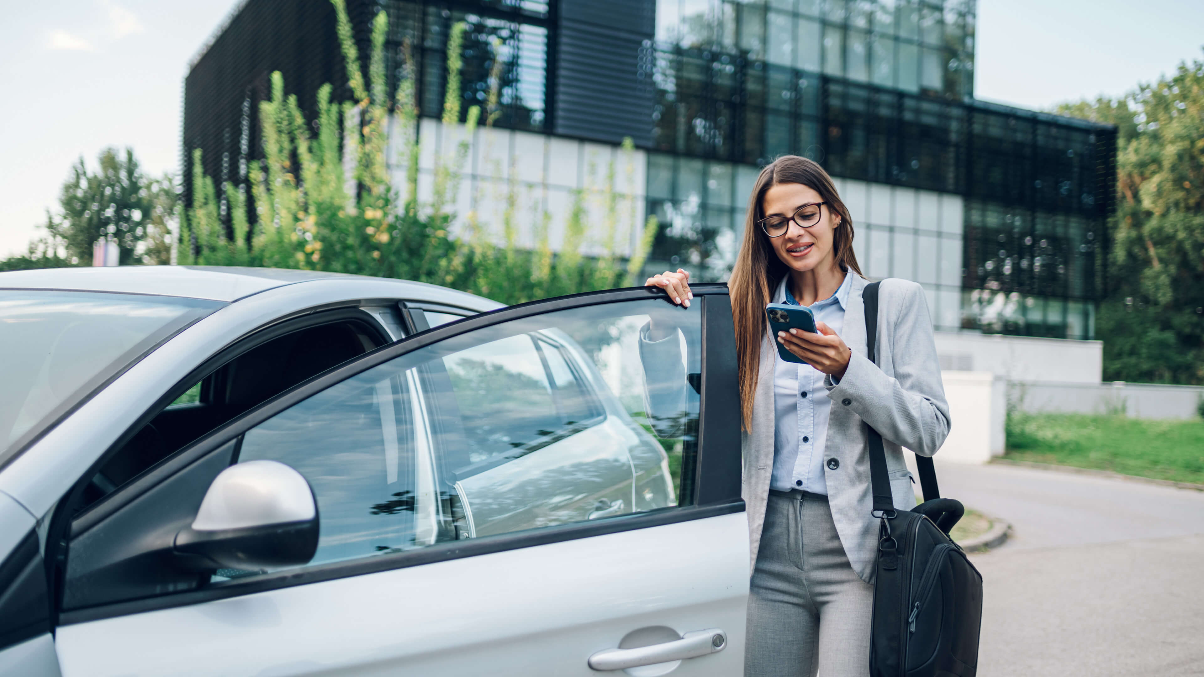 Frau am Auto mit Handy in der Hand