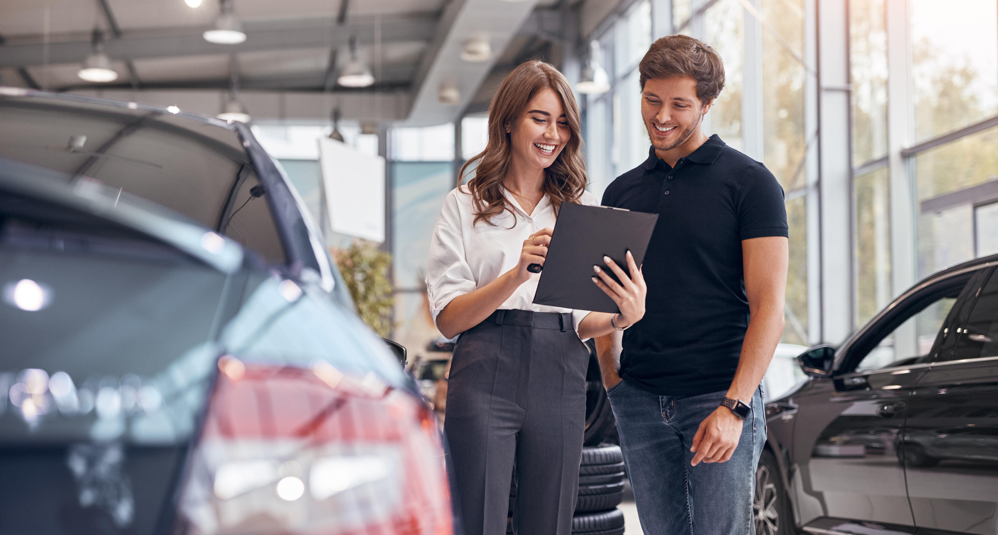 Eine Frau und ein Mann stehen in einem Autohaus und blicken zusammen auf ein Clipboard