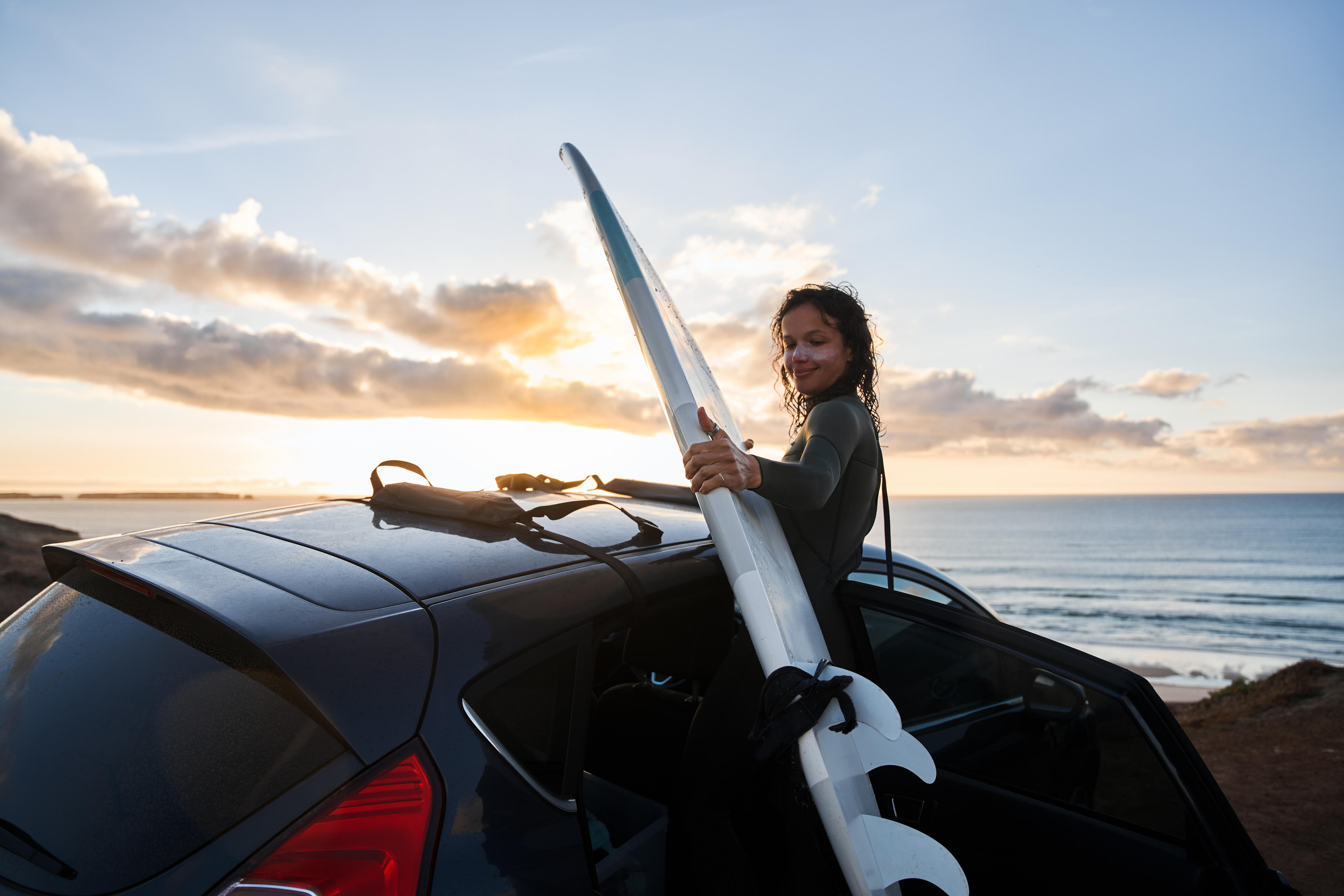 Eine junge Surferin möchte ihr Surfbrett auf dem Dach des Autos befestigen