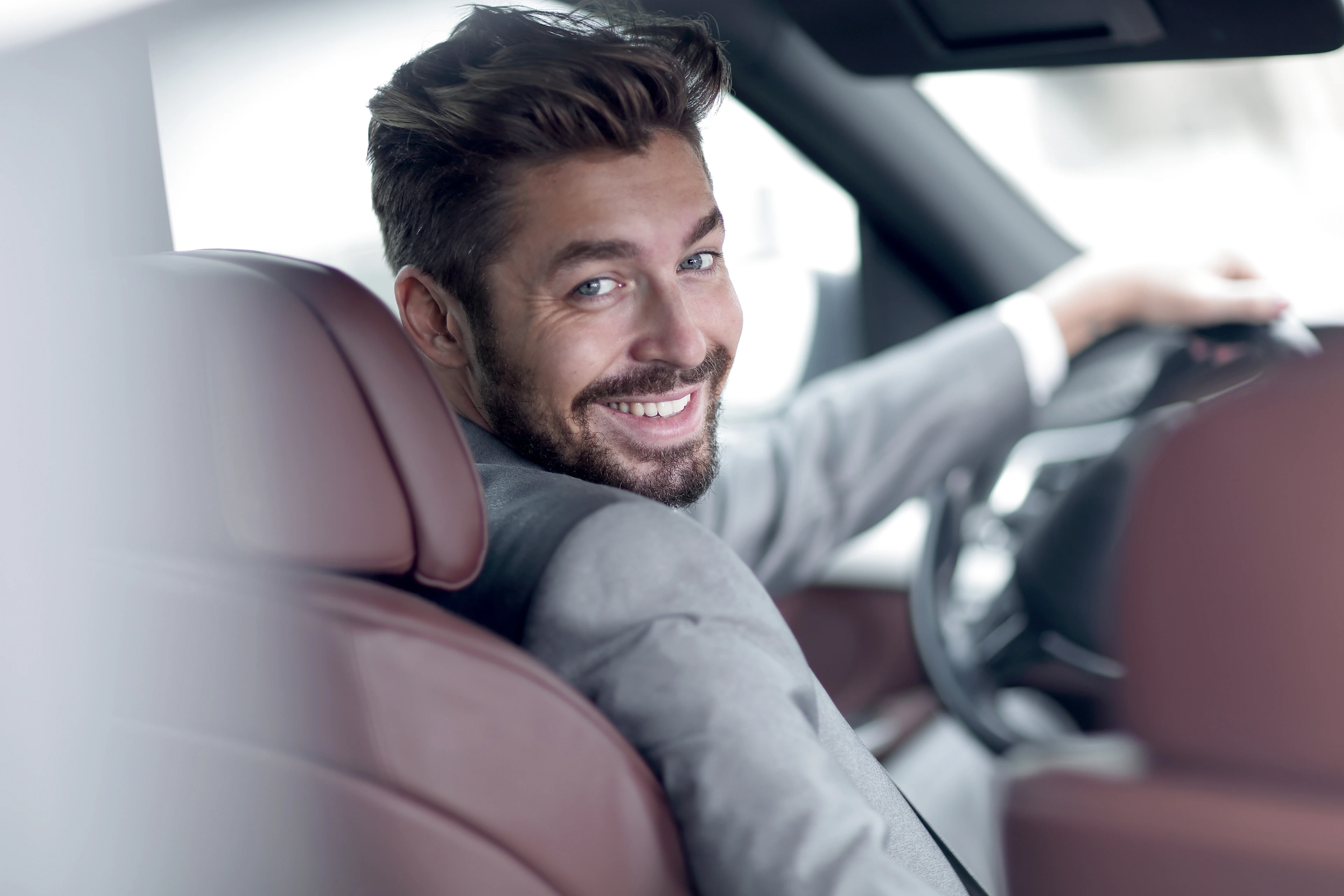 Mann mit Bart sitzt in einem Auto mit weinroten Ledersitzen