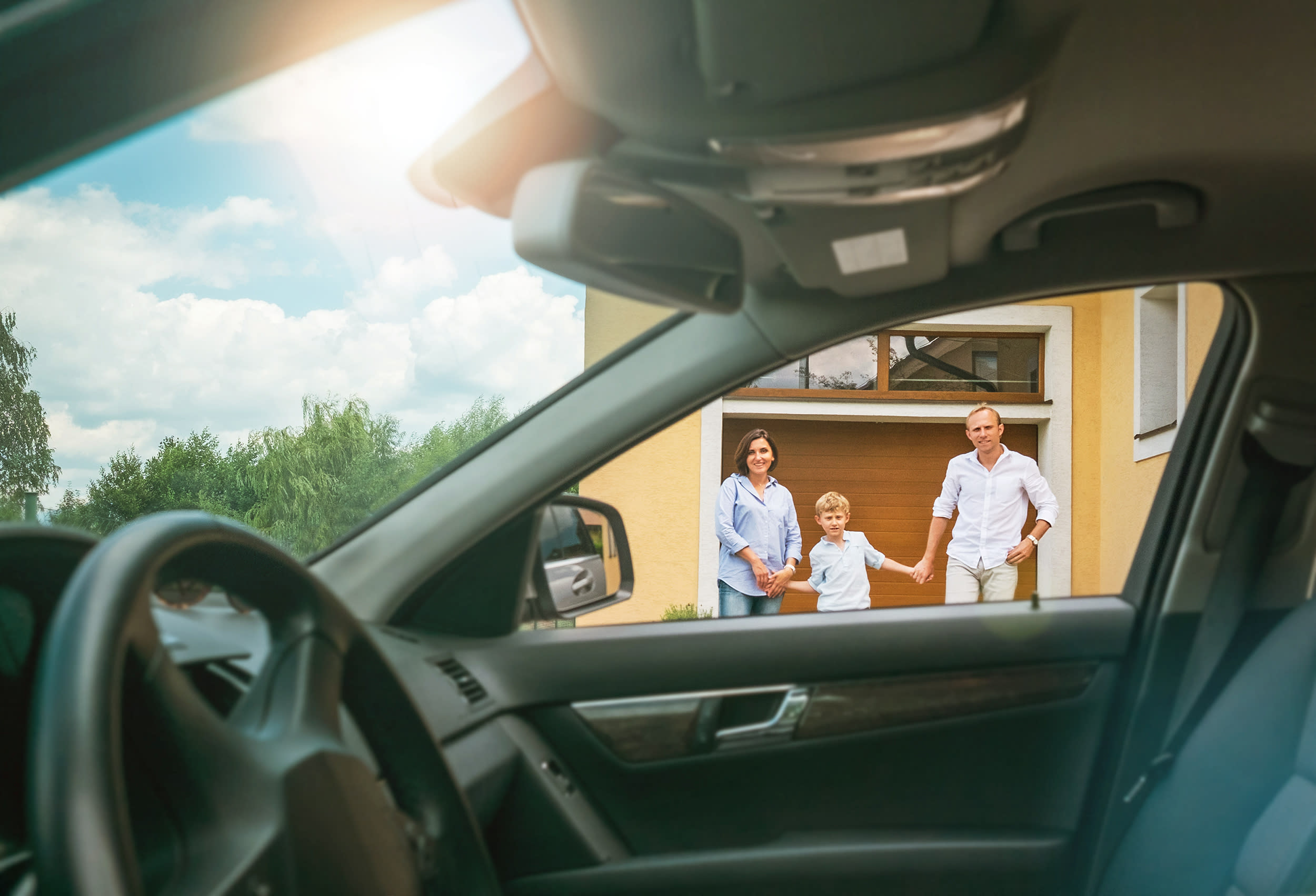 Durch das geöffnete Autofenster sieht man die Familie vor dem Haus.