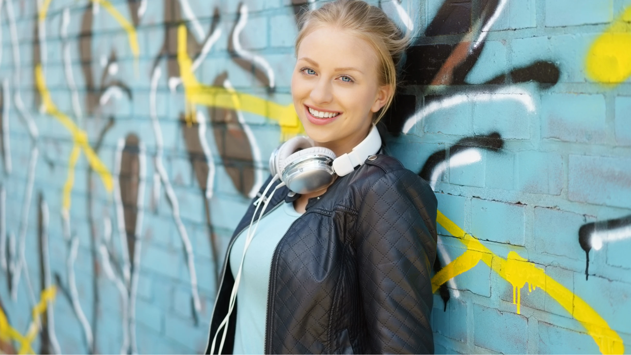Frau mit Kopfhörer lehnt an einer Graffitiwand