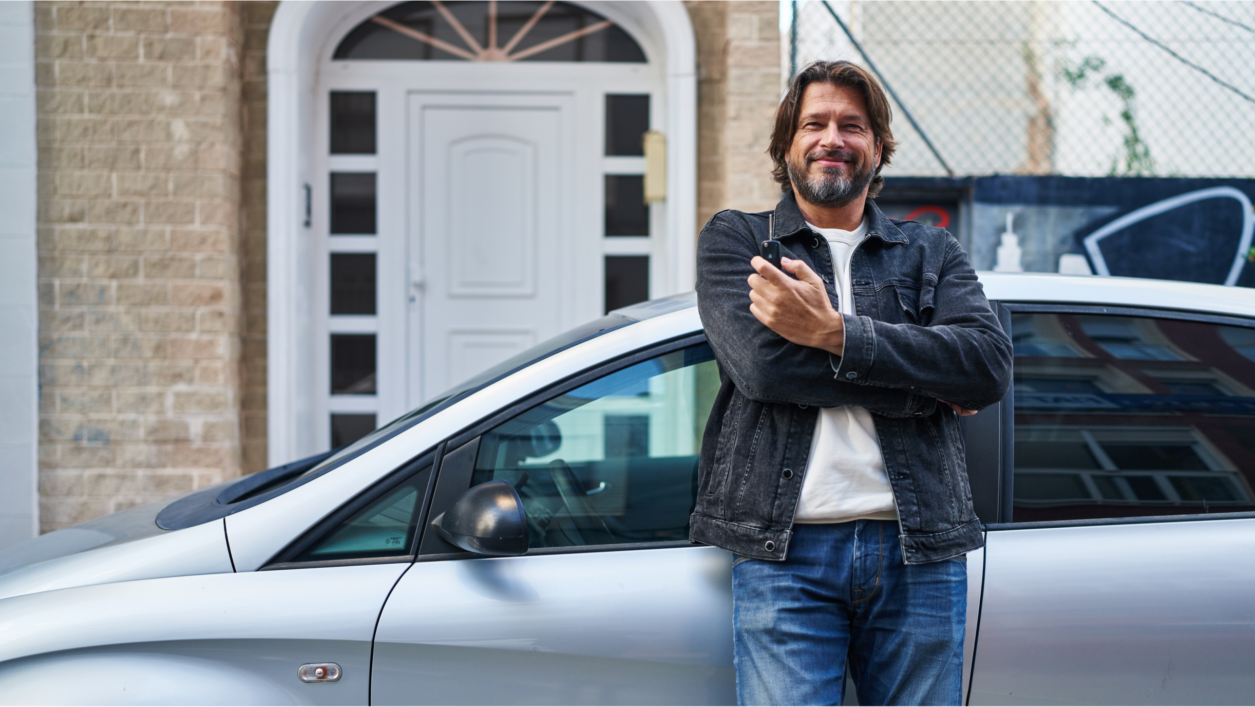 Mann lehnt an einem Auto vor einem Haus
