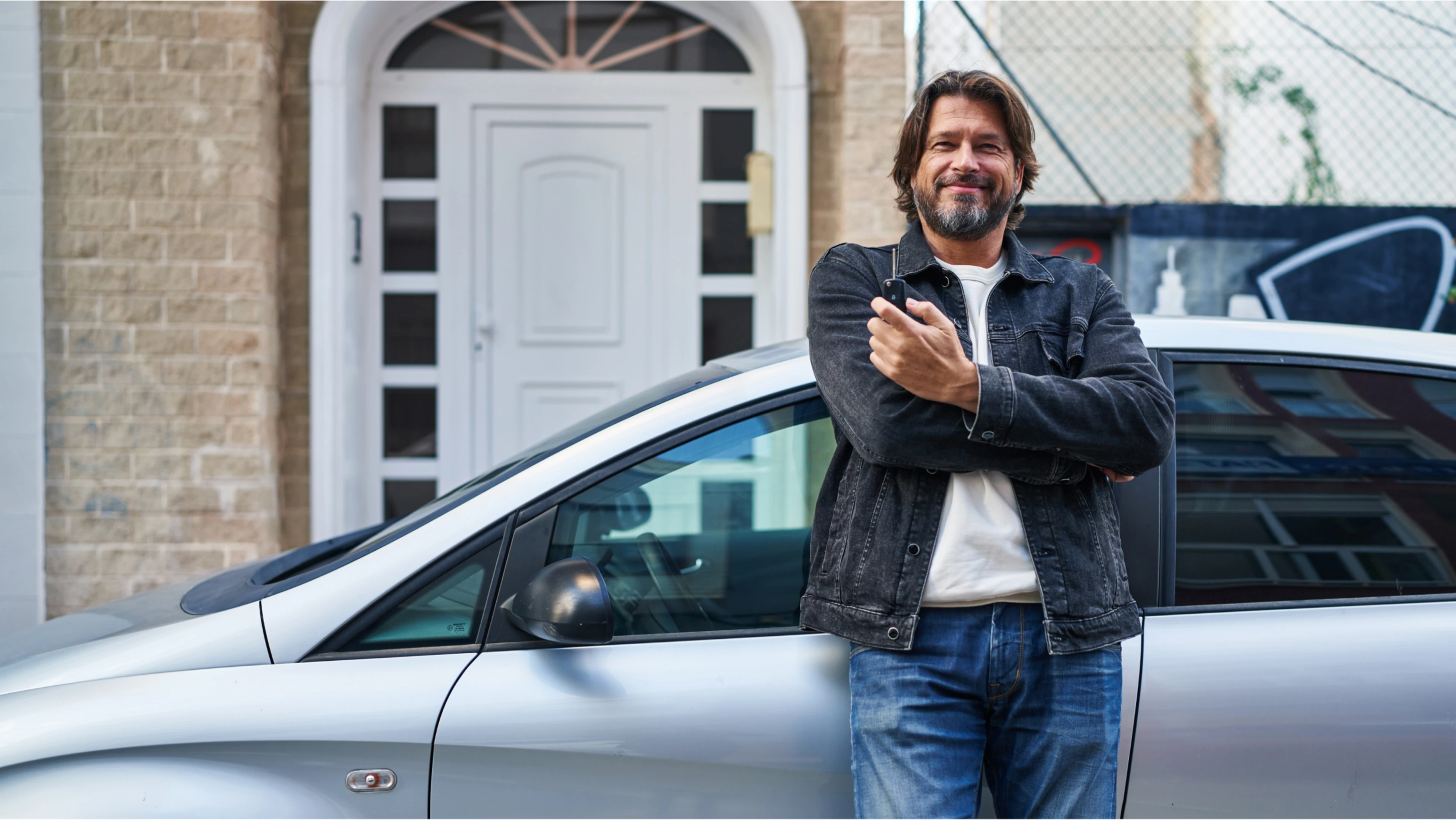 Mann steht vor einem Haus und lehnt am Auto