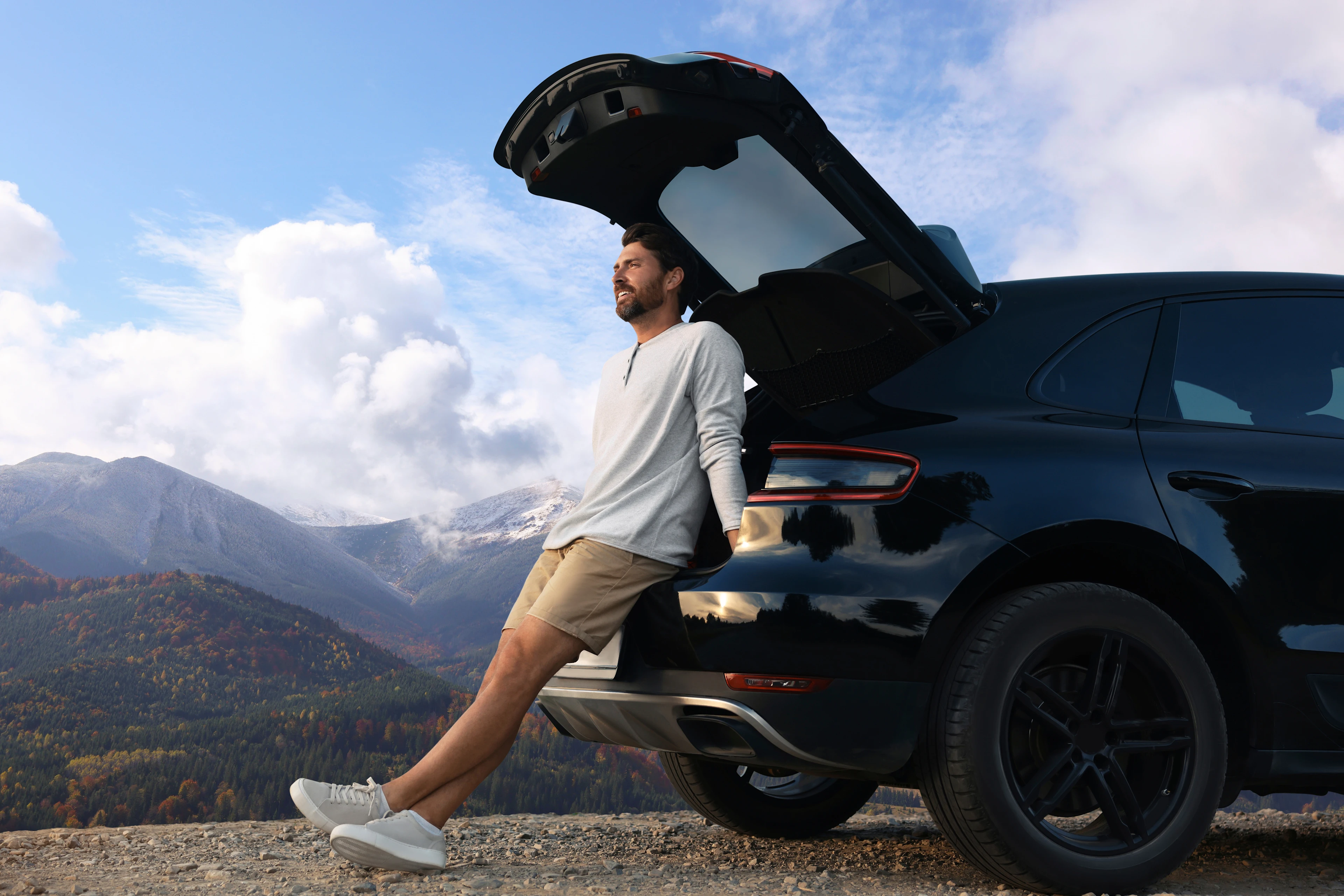 Ein Mann sitzt im geöffneten Kofferraum und blickt in die Landschaft