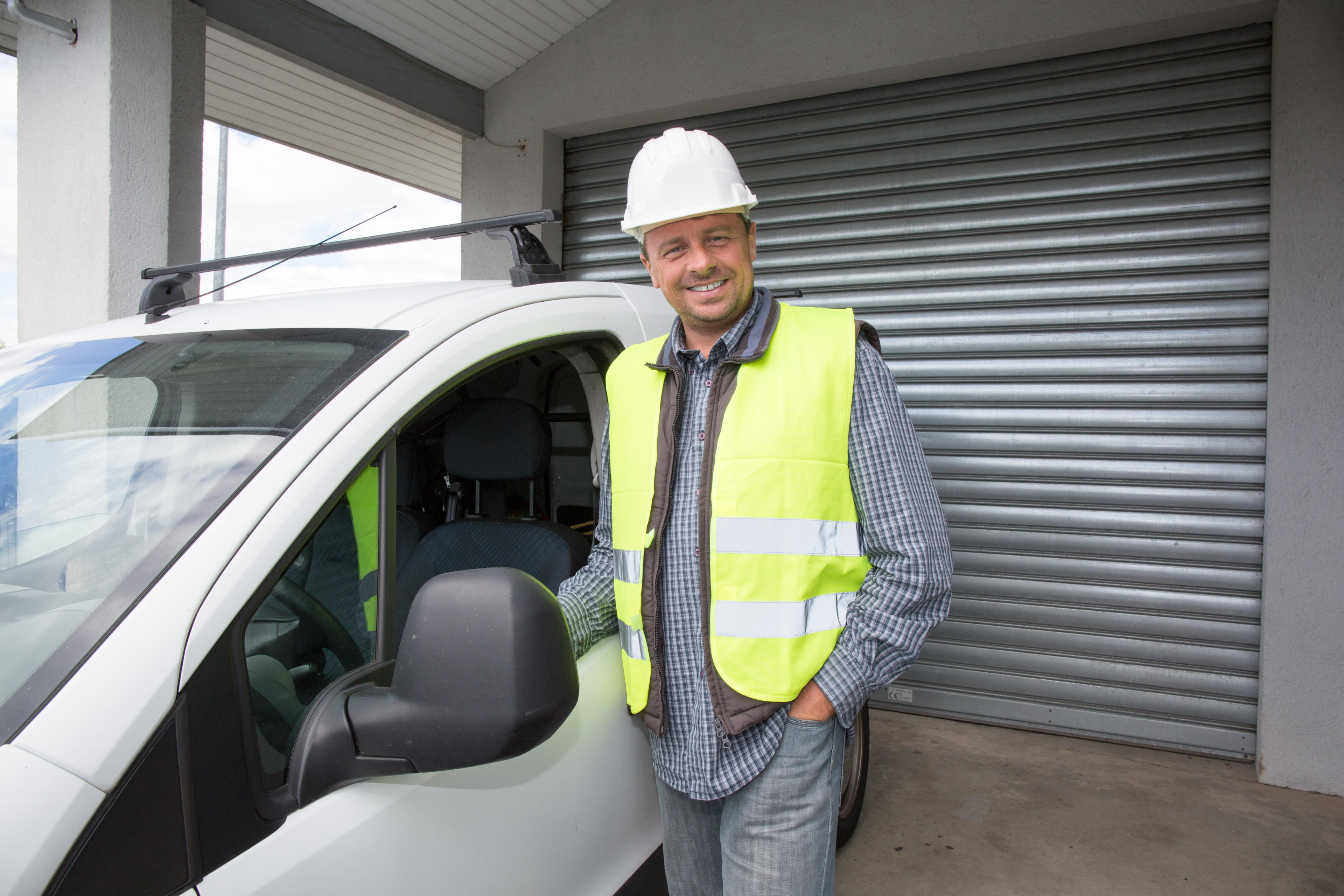 Mann mit Bauhelm und Warnweste steht nehmen einem weißen Kleintransporter