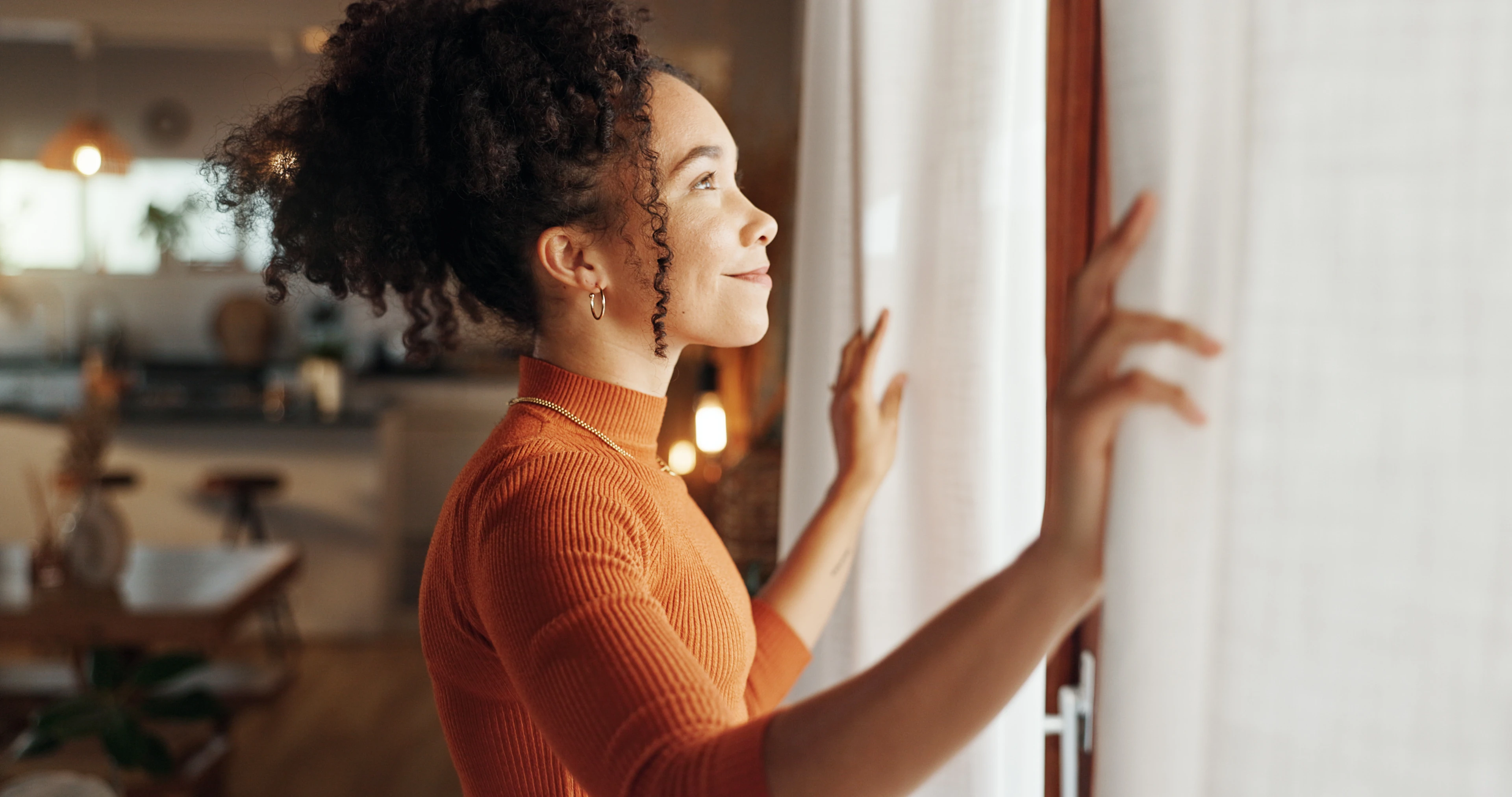 Eine Frau schaut mit hoffnungsvollem Blick aus dem Fenster ins Licht.