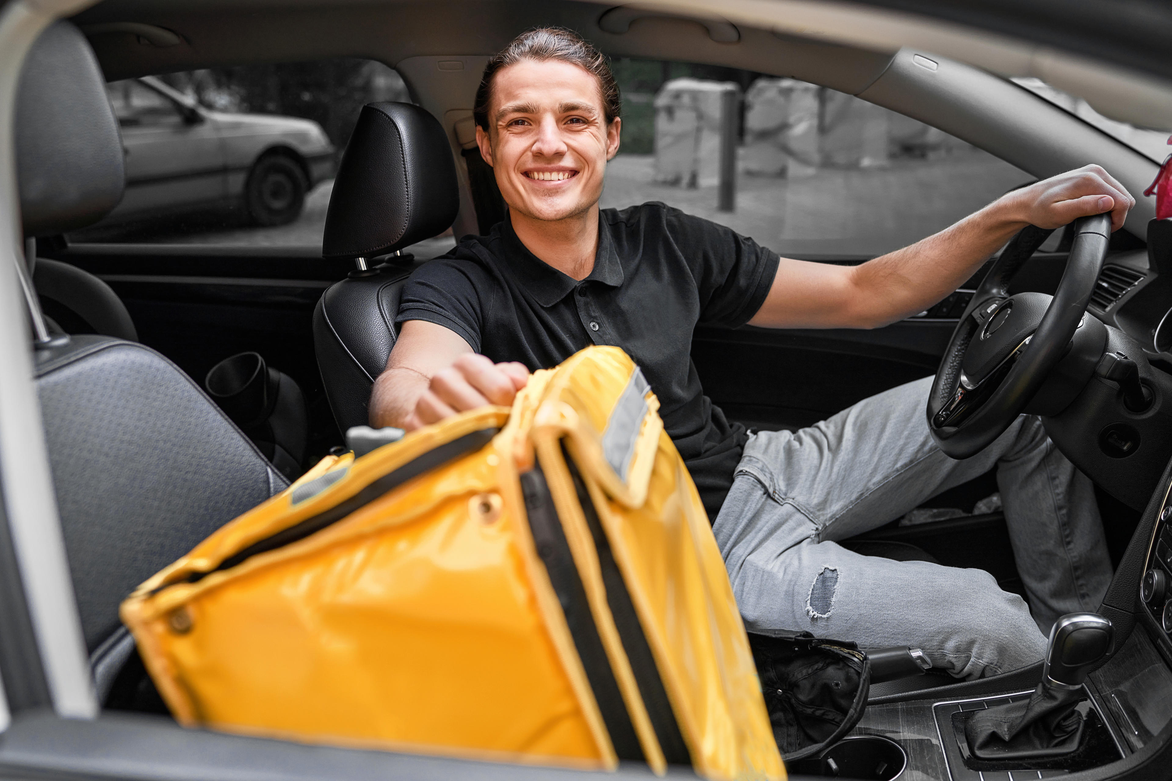 Mann sitz im Auto mit gelber Lieferdiensttasche auf dem Beifahrersitz