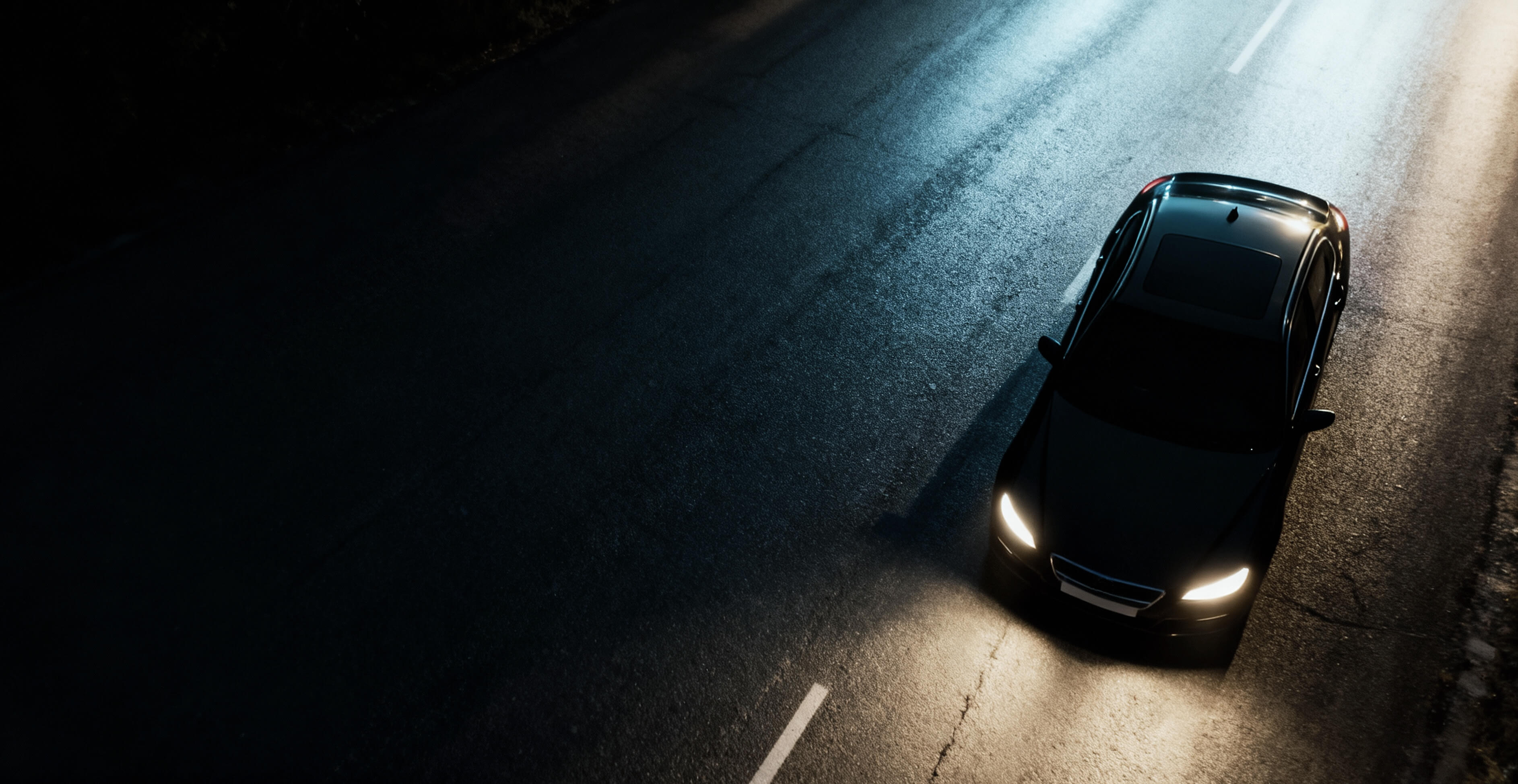 Dunkles Auto fährt Nachts auf nasser Straße mit eingeschalteten Scheinwerfern